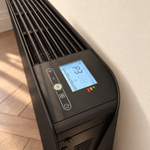 Gros plan du thermostat digital et de la grille du radiateur Molia noir dans un intérieur lumineux